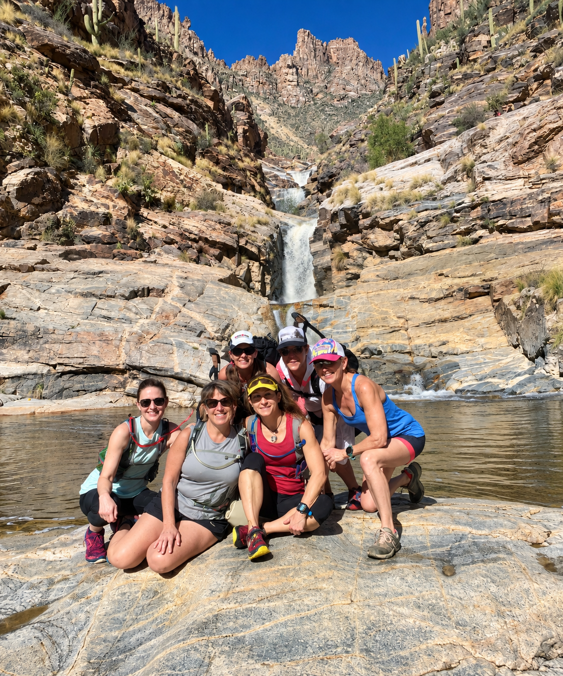 Women hikers posing by a desert waterfall in a rocky canyon